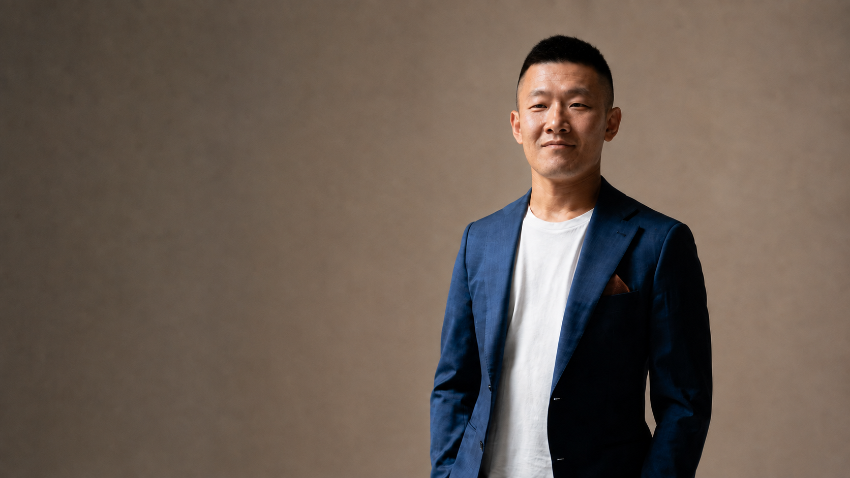 Don Chen in a blue suit against a warm neutral studio backdrop